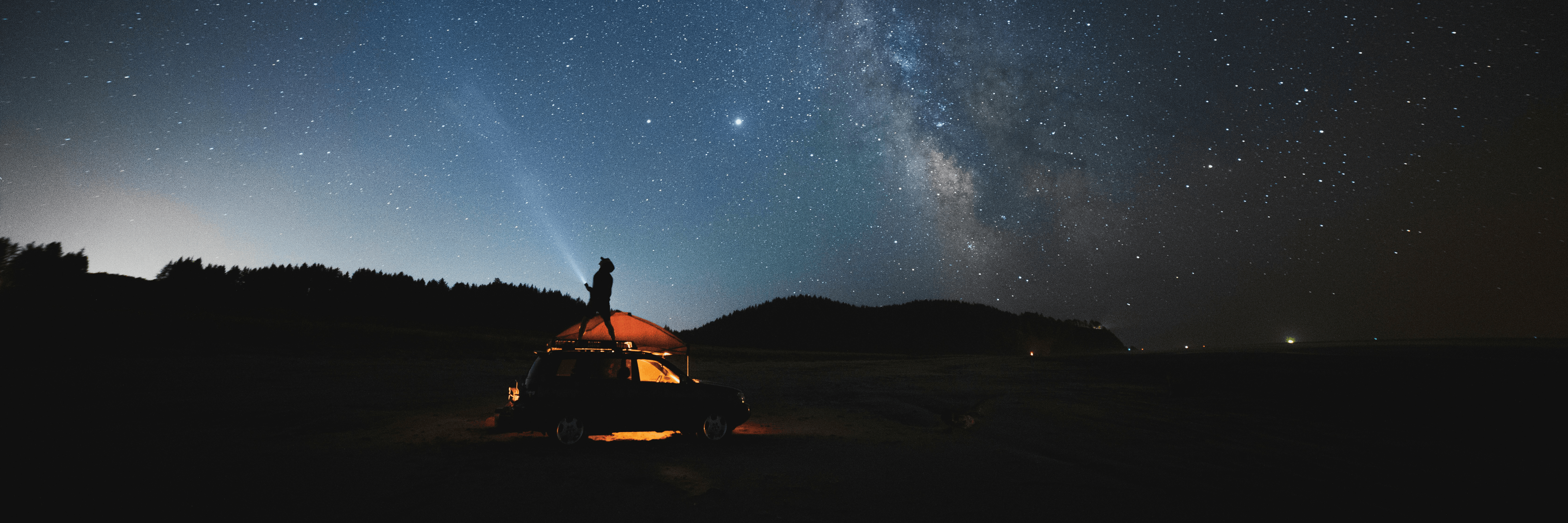 Car and tent set up under vast night sky