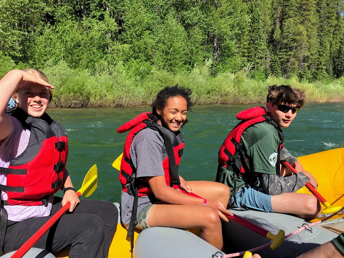 [Image Description: Three MCC youth crew members are sitting in a yellow raft, wearing PFDs, holding paddles and squinting in the sunshine on a river in Montana.]