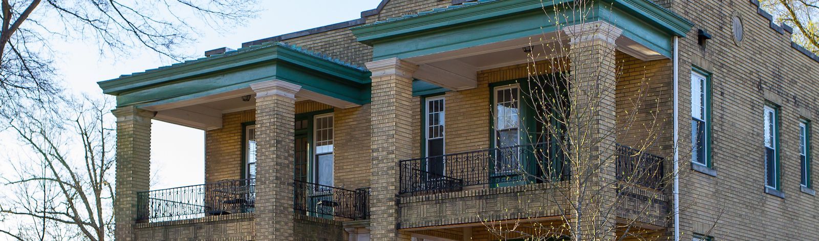 Exterior photo of Reinvestment Partners' main office building in Durham, North Carolina. The building is two stories, made of yellow brick, with dark green accents near the roof and on the window frames. This photo shows the building's top story, which ha
