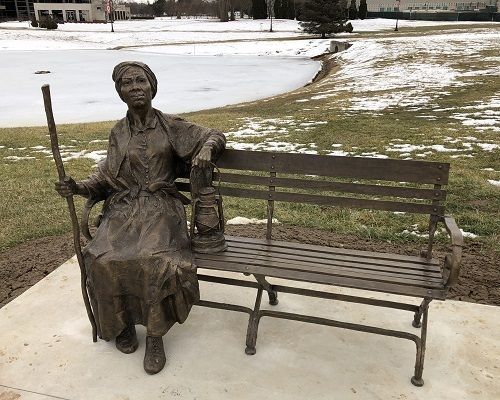 A bronze sculpture of Harriet Tubman sitting on a bronze bench is pictured on a snowy campus.