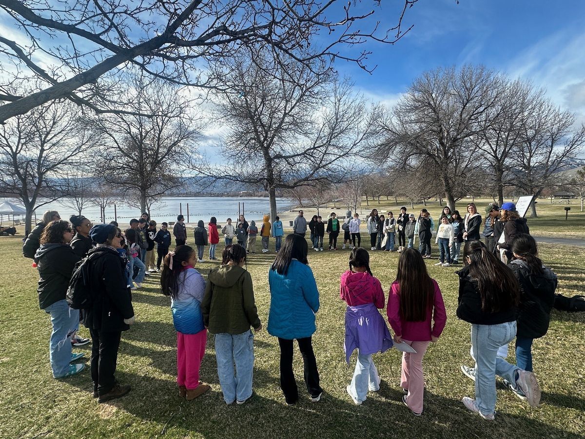 A large group of students convenes on the banks of the Columbia River before their lesson.