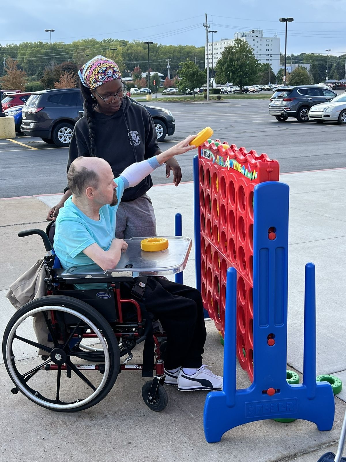 An aide helps a man in a wheelchair to place a piece into a large Connect 4 game.