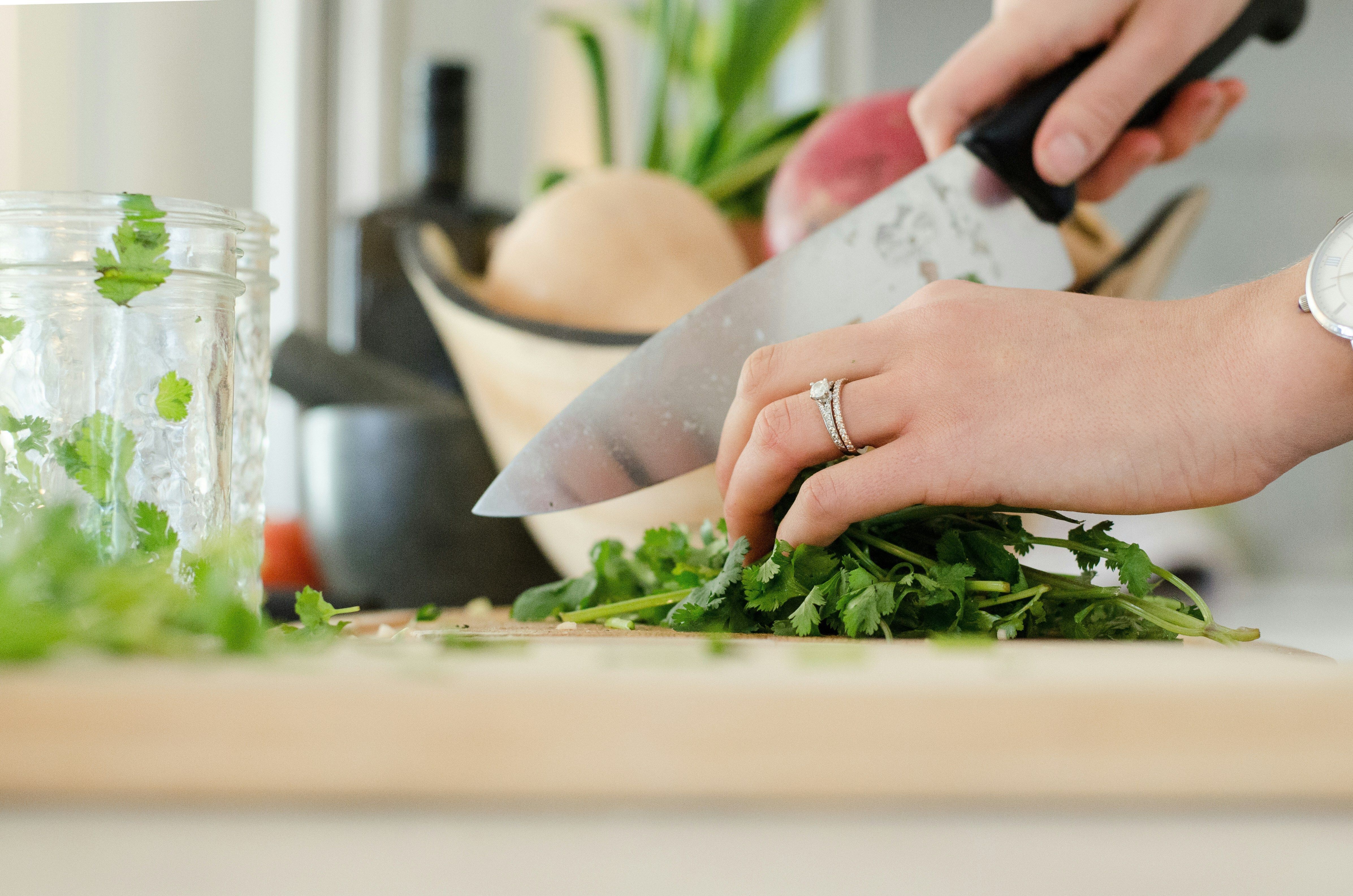 Image of hands holding a knife and chopping herbs on a cutting board
