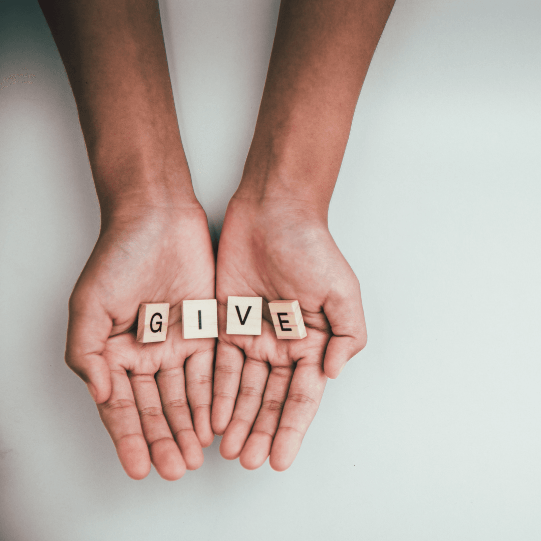 Hands holding scrabble pieces that spell "G-I-V-E"