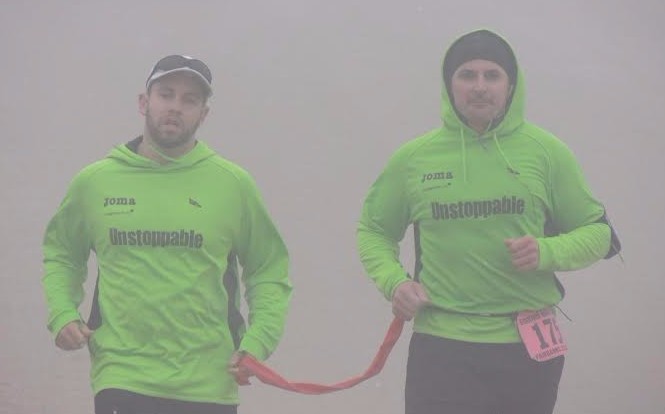 Picture of Brian Switzer and his Guide Marco running while wearing green sweatshirts that read: Unstoppable
