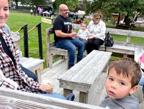 boy sitting in a large wooden wagon looks up at the camera while he waits for a ride