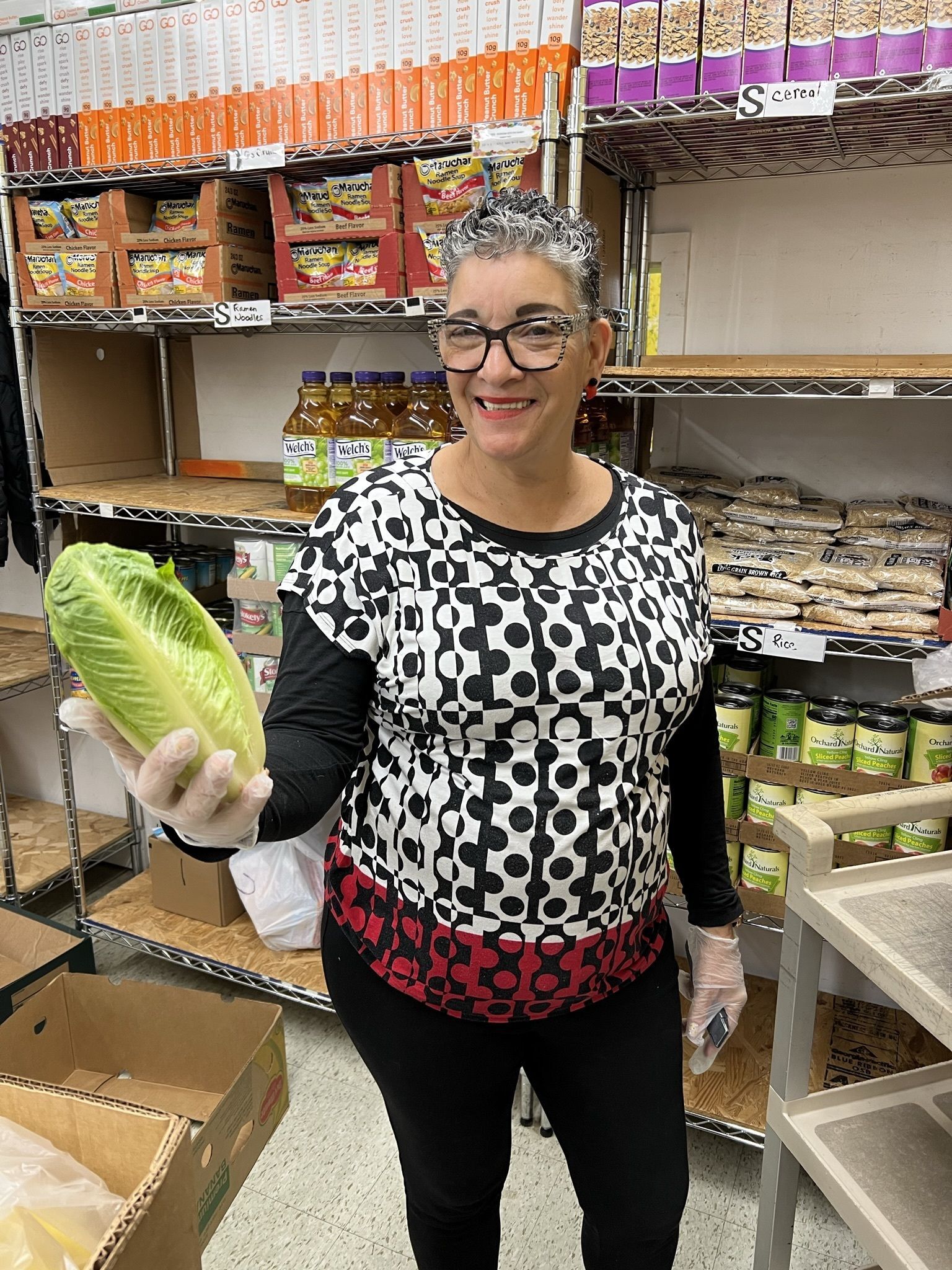 A lady is holding a head of lettuce in her hand while smiling for the camera.