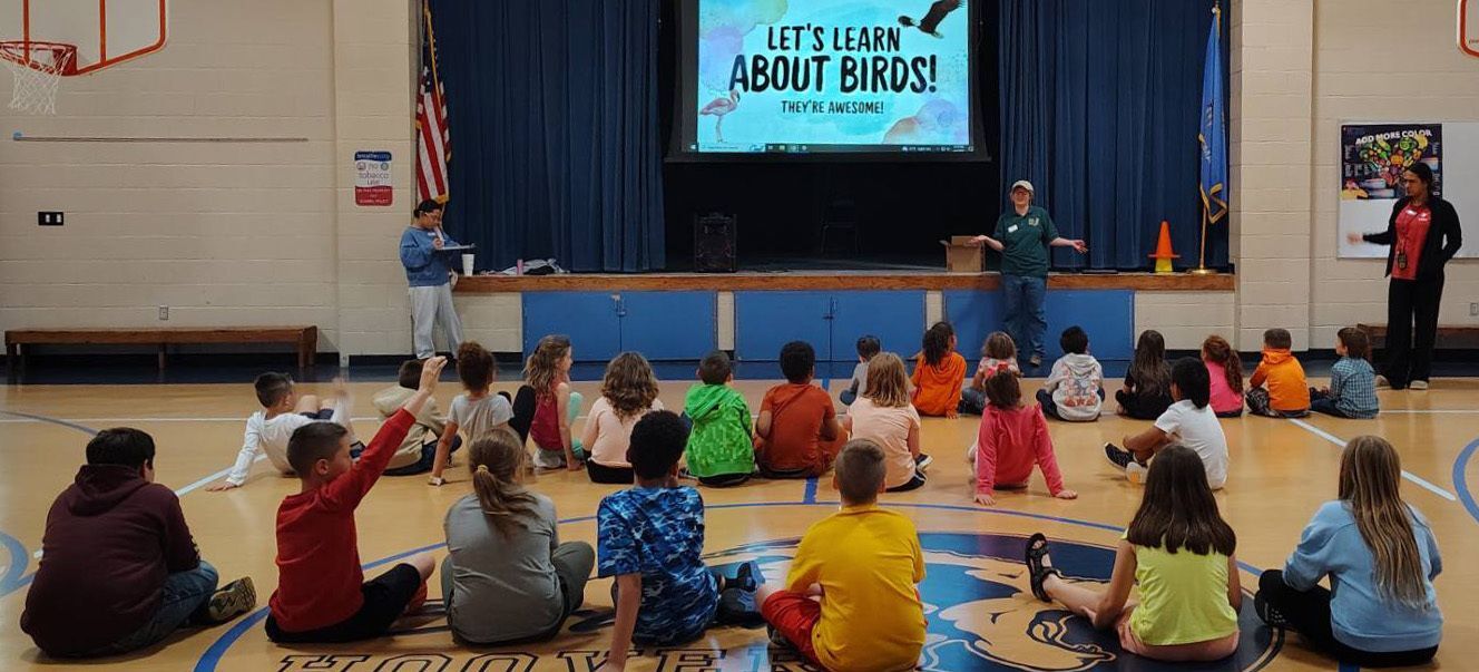 A Sutton Center educator presenting with an ambassador bird to a group of students during an elementary school visit.