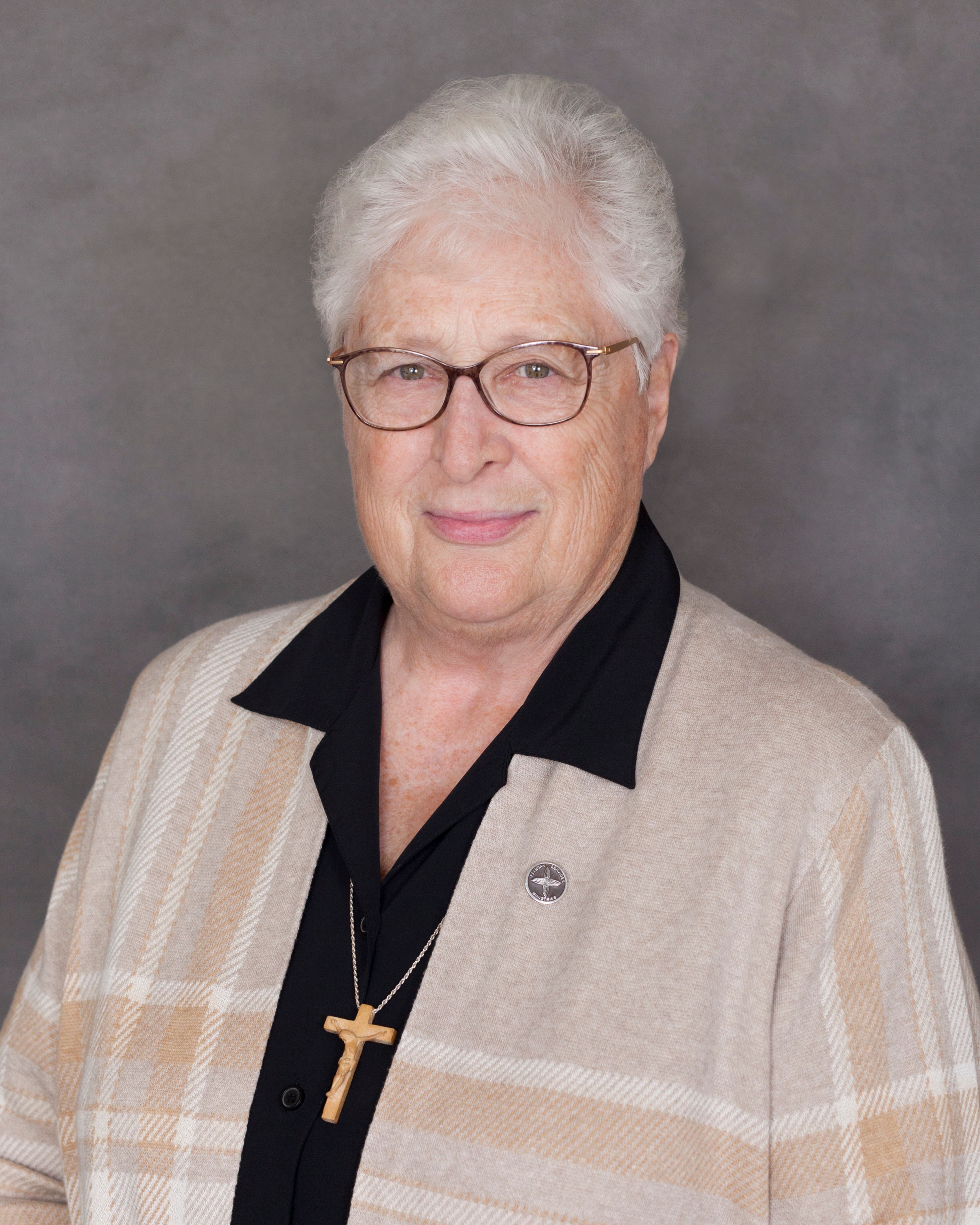 Sister Clarette wears a black collared shirt and tan sweater. 