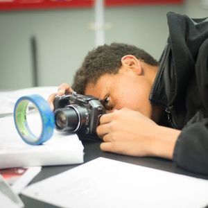 Young boy using a camera to take a picture through a roll of tape that is standing up.