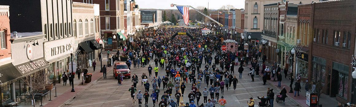 Crowd of runners on main street at start of race surrounded by historic buildings on each side.