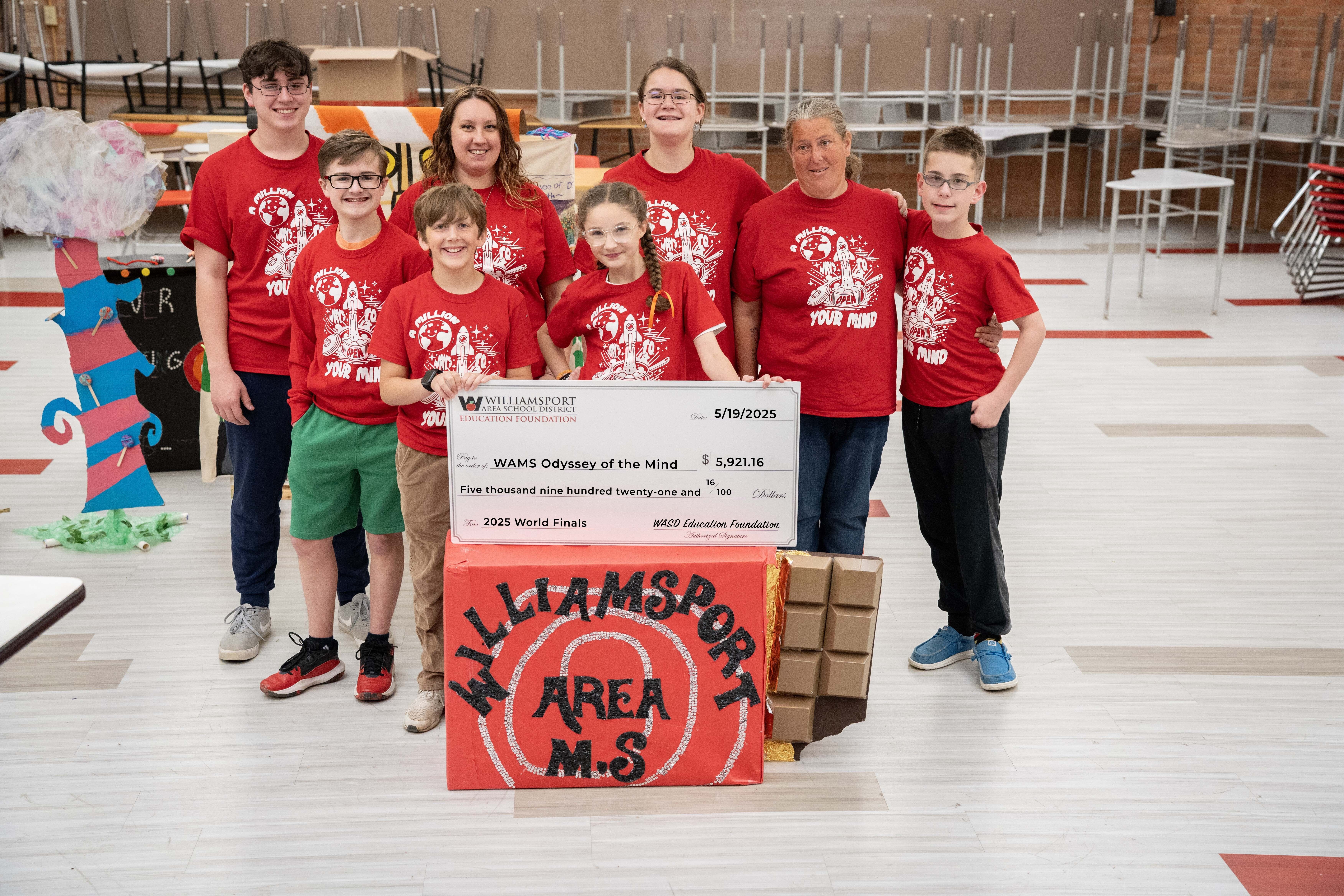 A photo of the OM team with their coaches holding a giant check.