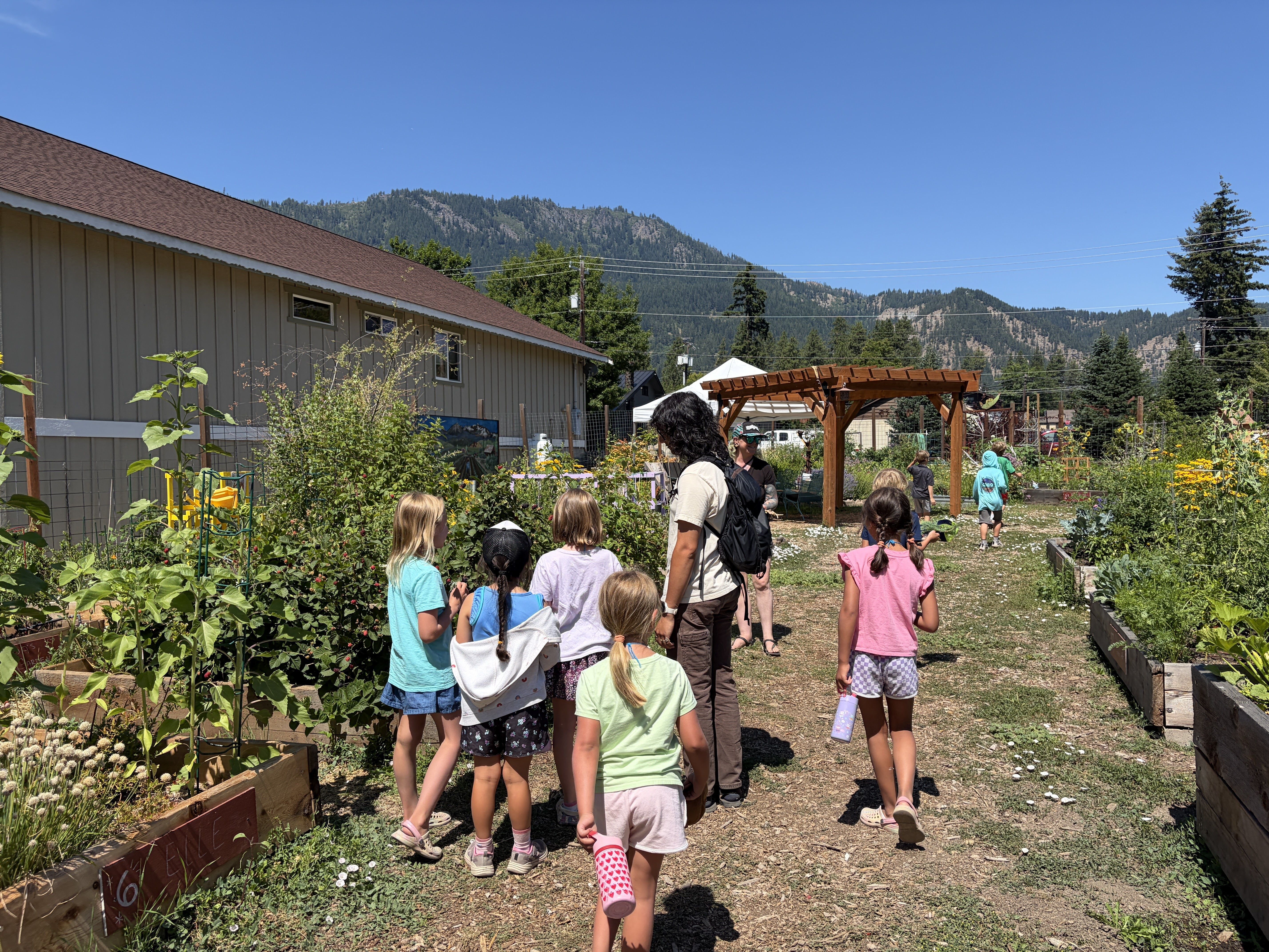 Image of educators and students in a garden holding up produce from the Soil to Snack youth camp.