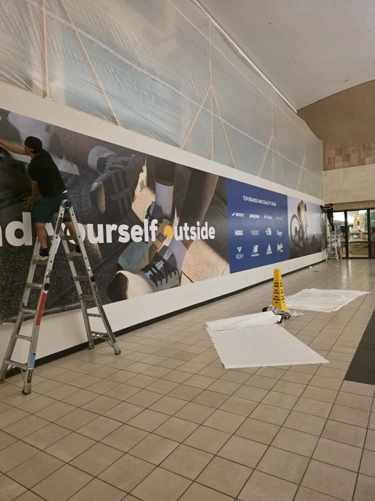 Two technicians from the install team using a boom lift to mount business signage panels on a multi-tenant pylon sign at 9000 Commerce Center under daylight conditions.