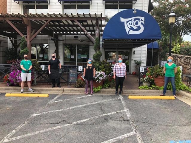 A photo of the Trio's restaurant storefront with members of their staff standing six feet apart from one another and wearing masks