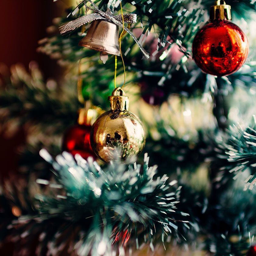 Close-up of shiny Christmas baubles and a bell on a green tree.