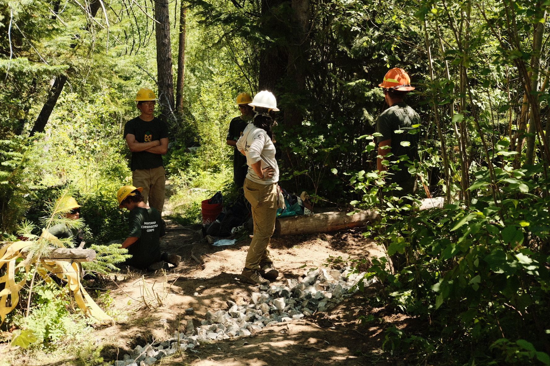 A youth crew stands listening to a project partner and crew leader give instruction.