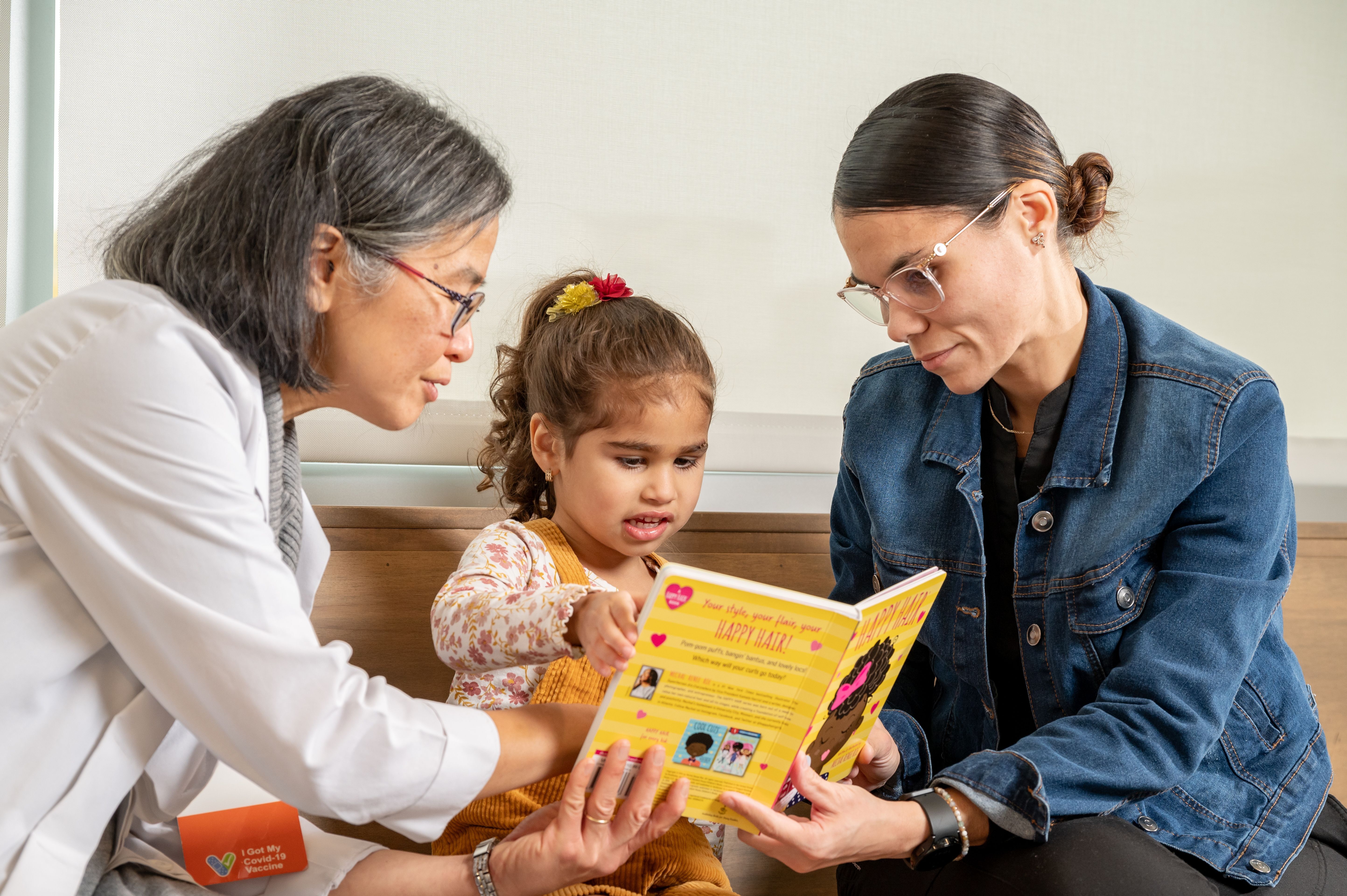 physician, young girl, and mother read big yellow book together 