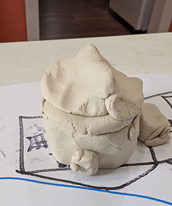 Clay house sculpture with roof on, placed on a hand-drawn community map