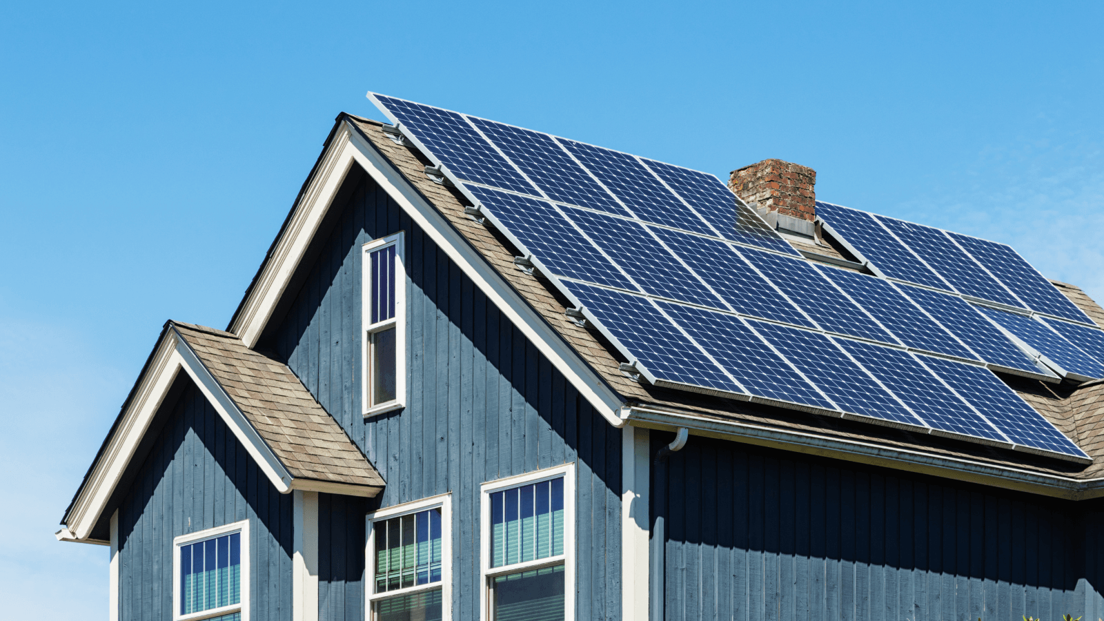 a blue house with solar panels on the slanted roof against a clear blue sky 