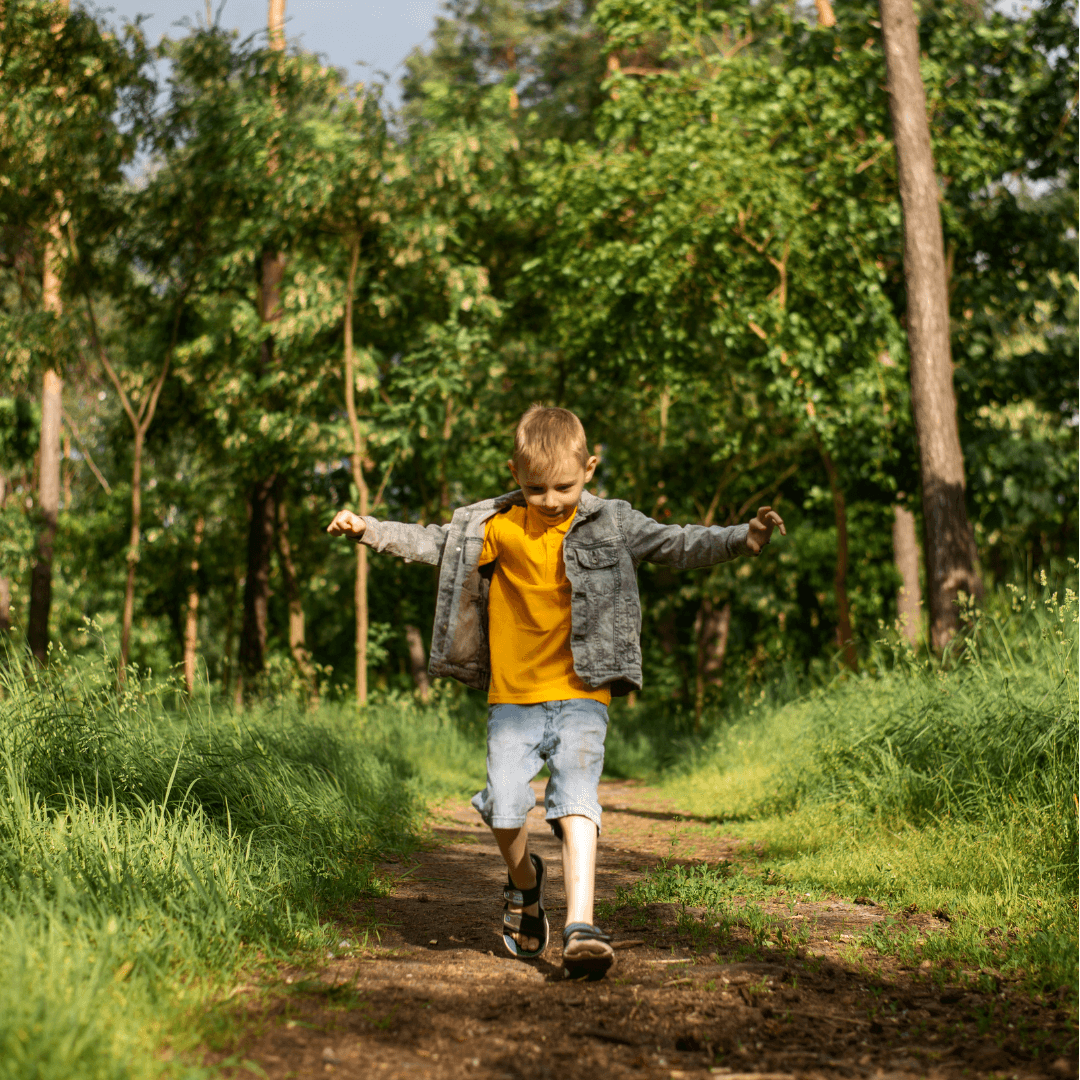A young boy joyfully walks down a dirt path in the woods. 