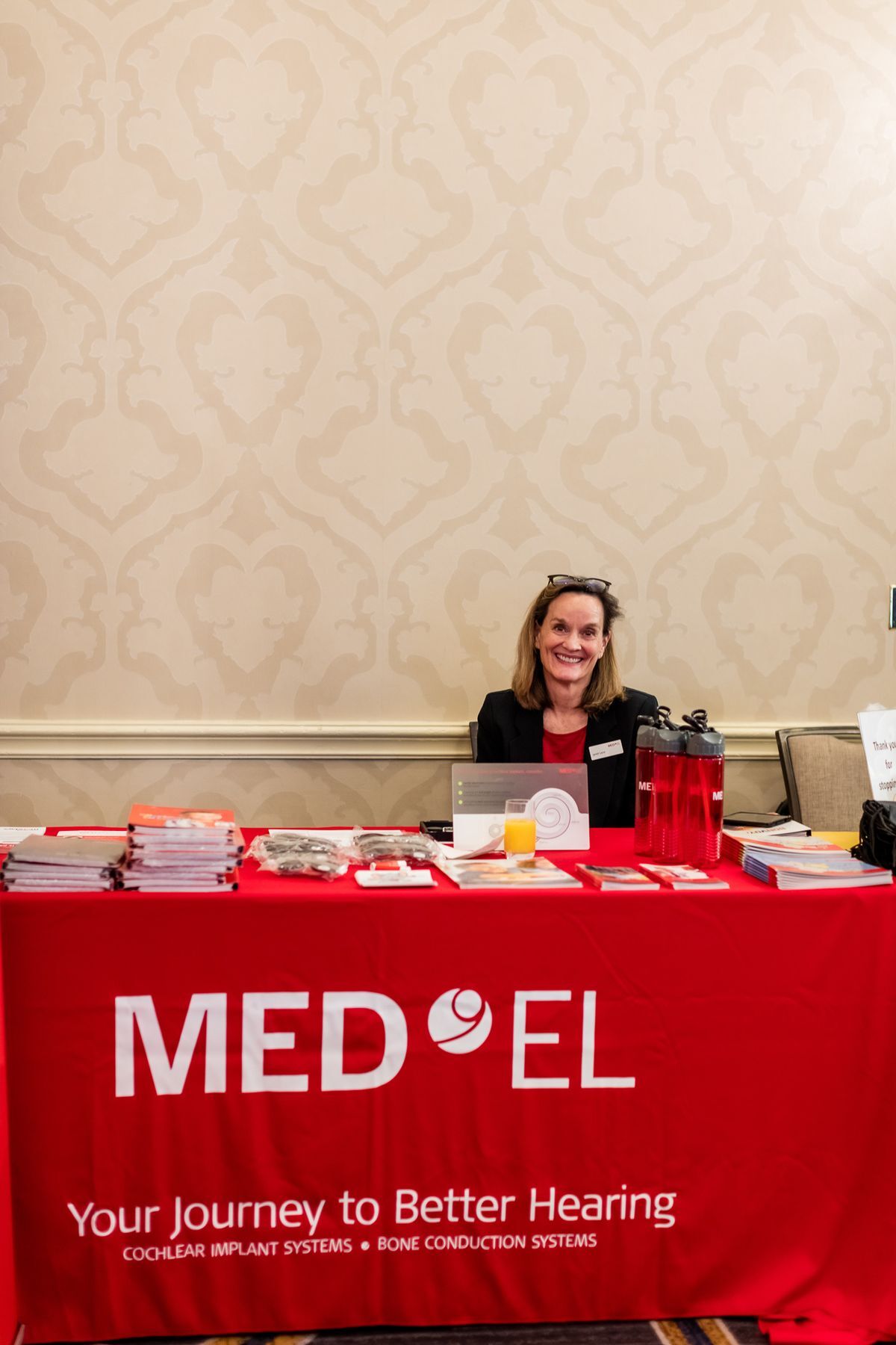A MedEL representative sitting at a table with a red MedEL cover.