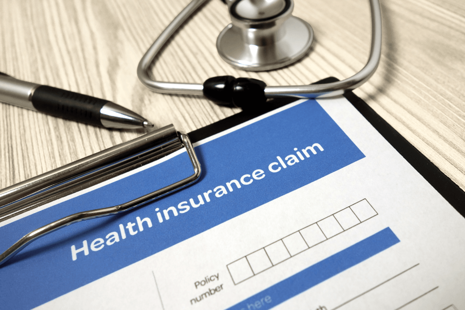 Health insurance claim form with blue and black text sits on a clipboard next to a stethoscope and pen