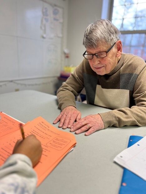 Adult with glasses sits across from a student working on homework