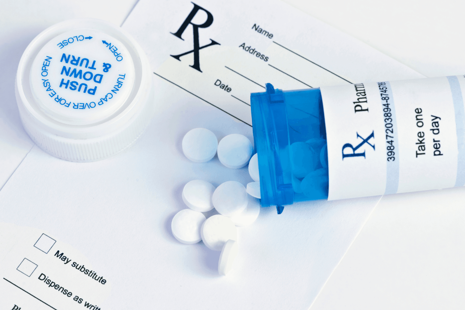 Open blue prescription bottle on its side with several white pills spilling out on top of white RX prescription pad