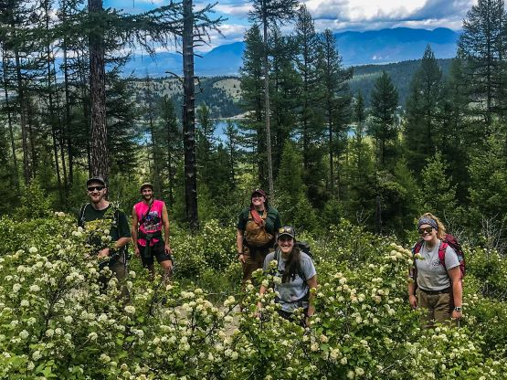 [Image Description: Northern Rockies staff standing in a field of flowers above a lake, all on a hike.]