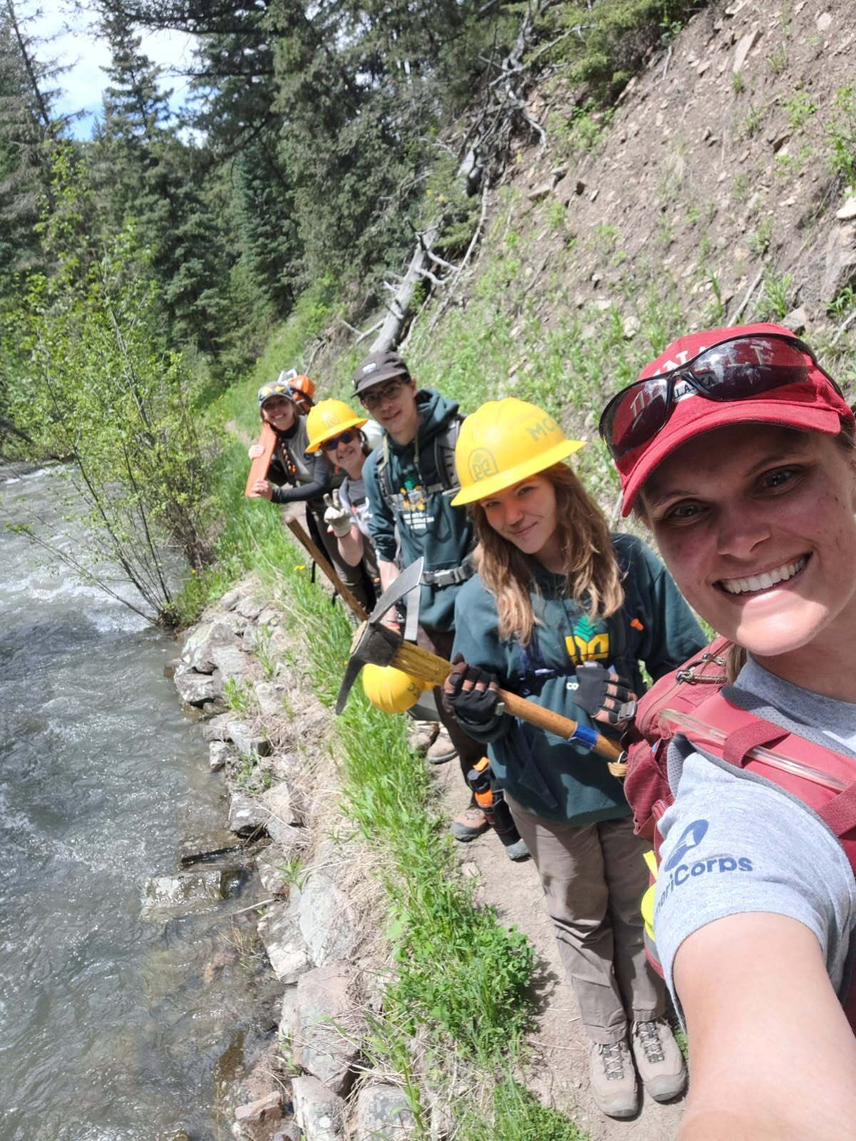 A crew stands on a trail besides a creek, taking a selfie.