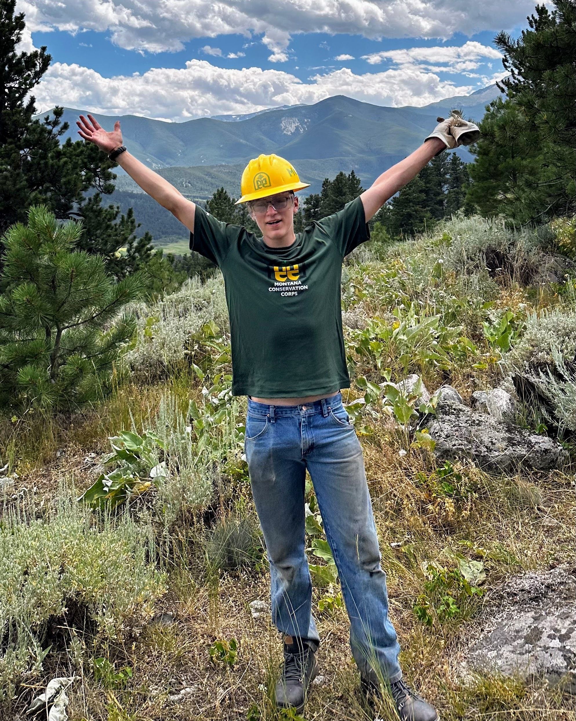 A crew member smiles with their hands over their head in front of a scenic view