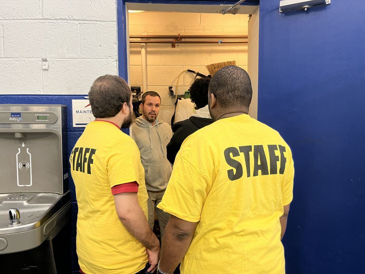 Two adults looking inside the closet of their new job as they learn about what their duties are.