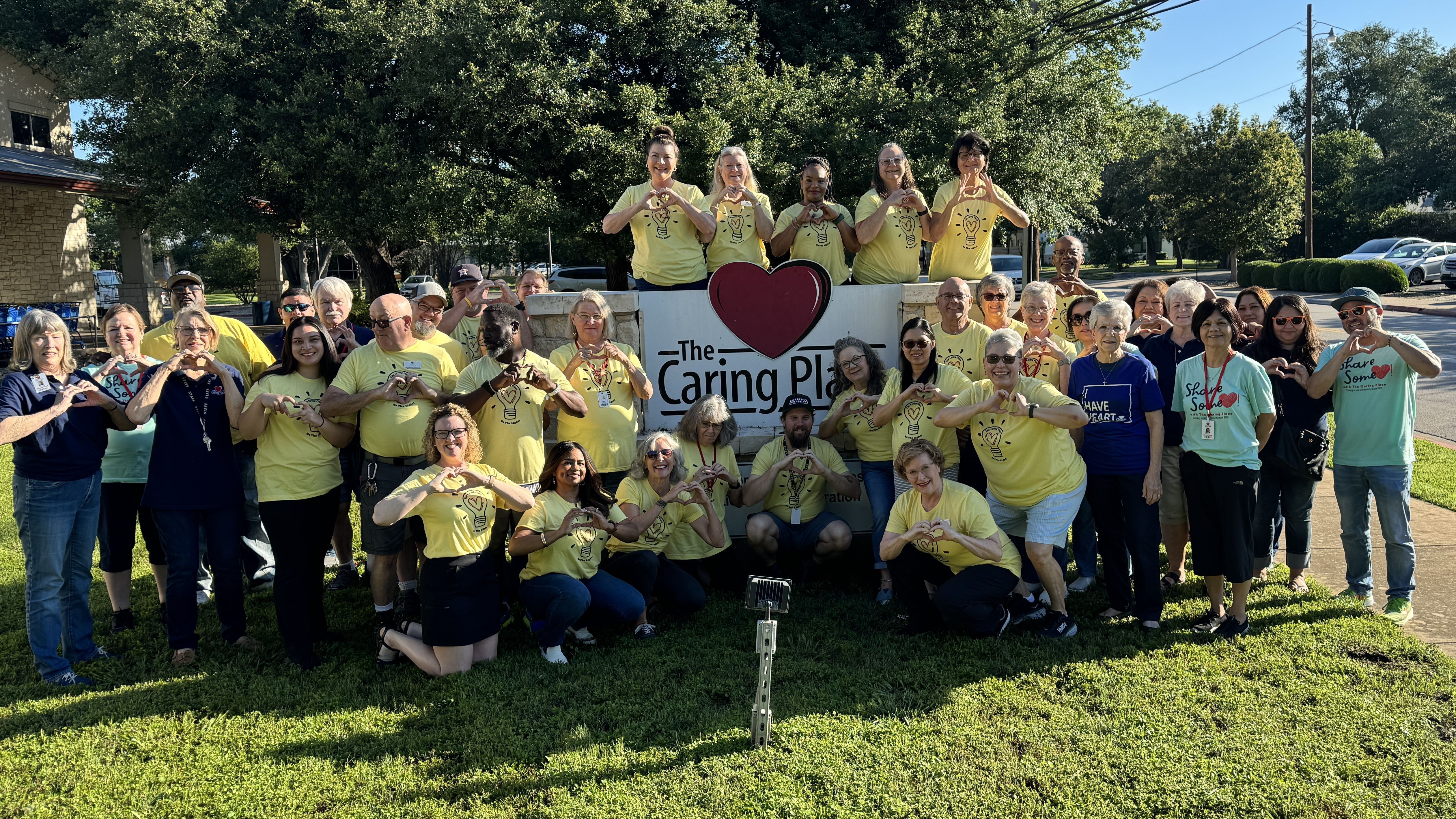 The Caring Place staff and volunteers stand outside of the main building making heart symbols with their hands