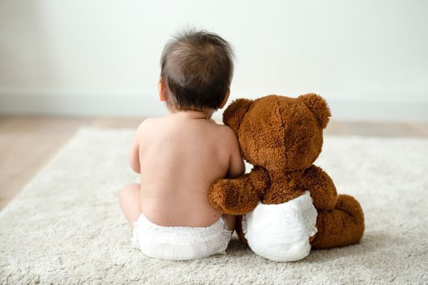 baby sitting with teddy bear, both wearing diapers