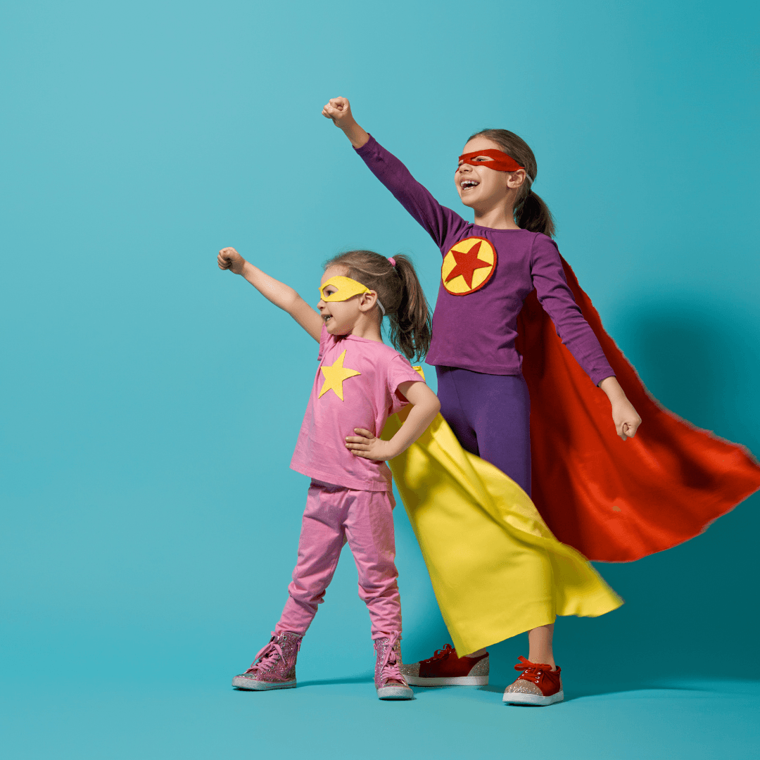 Two girls dressed up as superheroes put their right fists in the air like they are about to take off