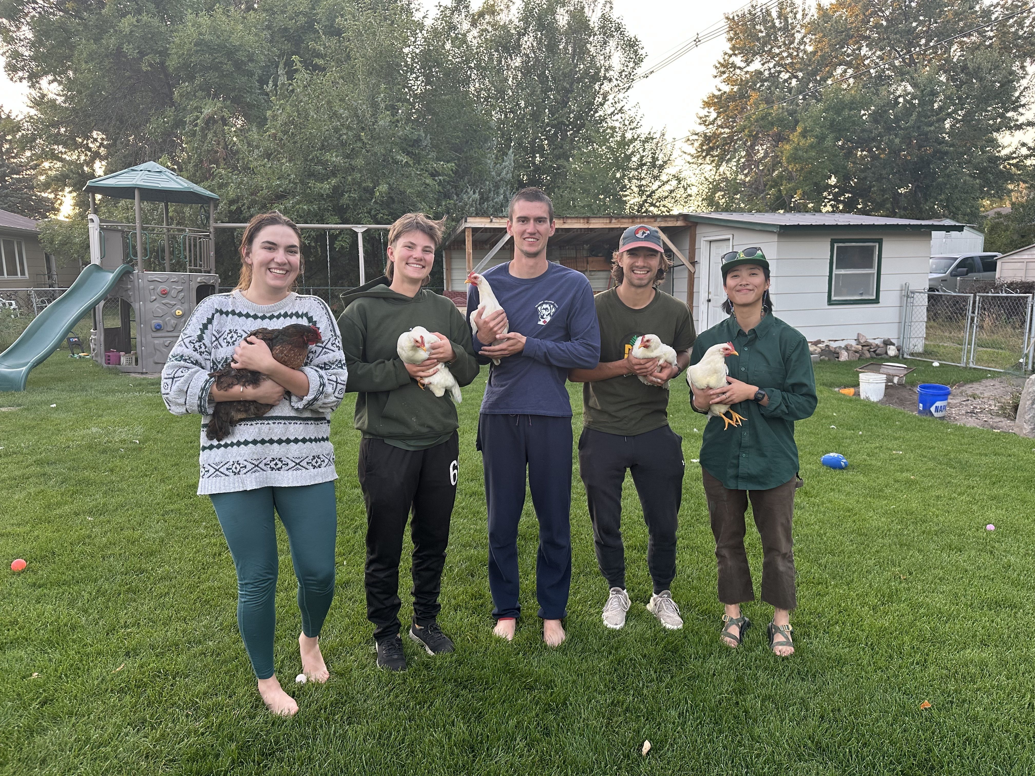 The crew stands in a backyard, holding chickens