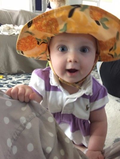 Photo of 1 year old Emma wearing a yellow sun hat and big smile on her face.