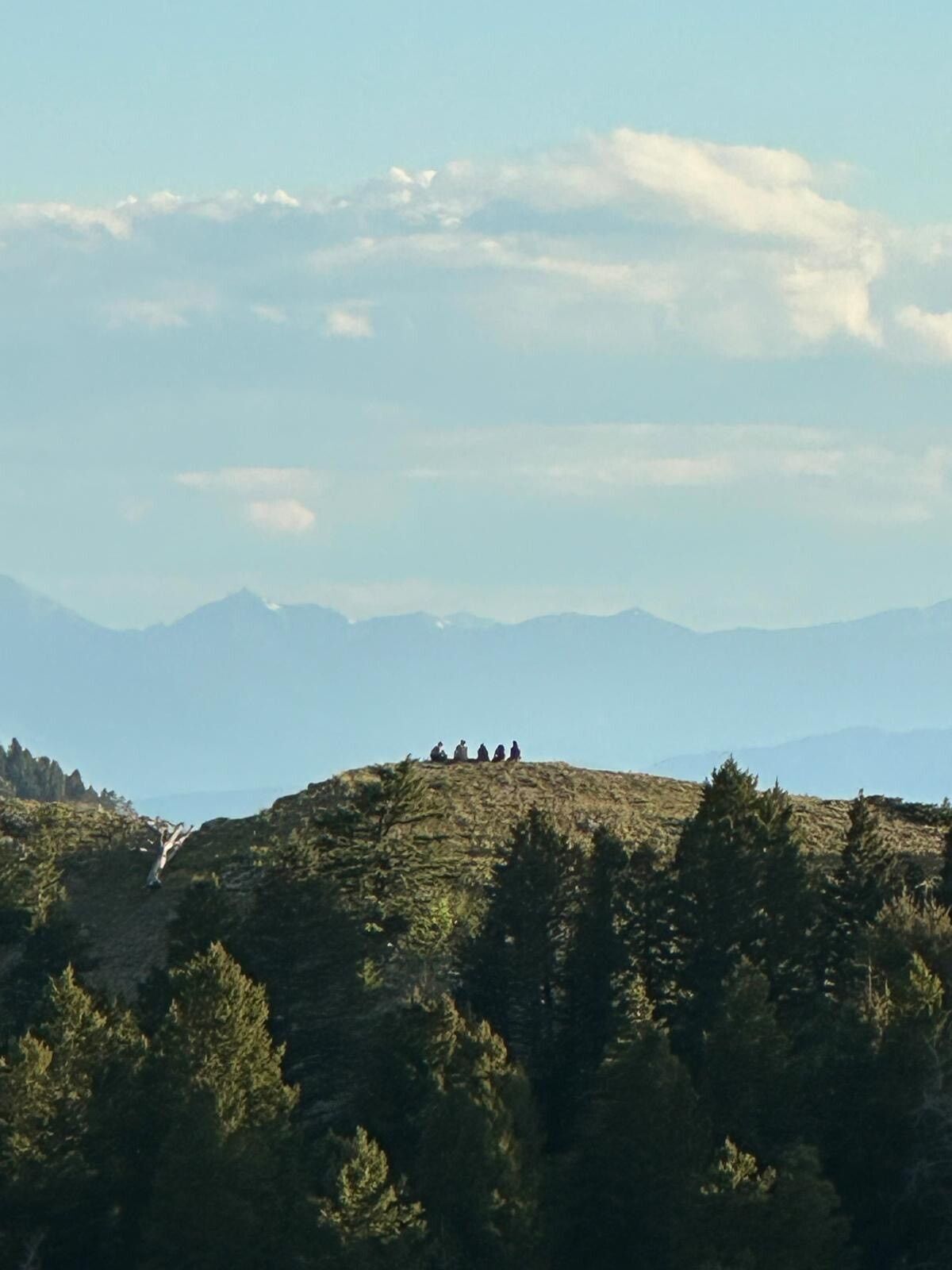 A shot of a rolling green hillside, with a crew of members sitting down far in the distance