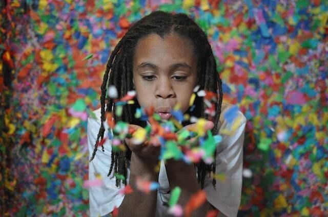 Young black girl blowing multicolored confetti from her hands