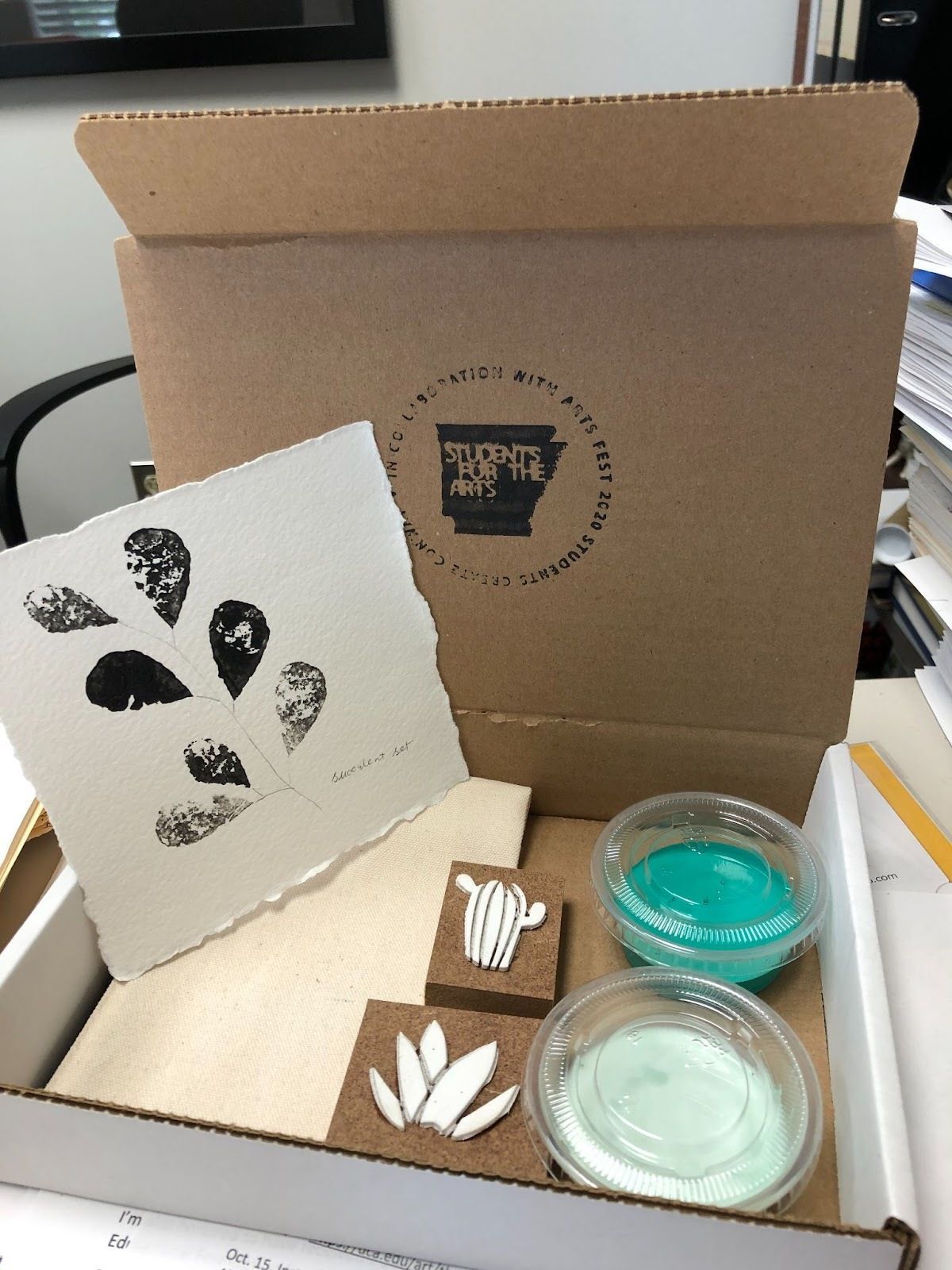 A Students for the Arts branded box contains supplies for a self-care arts project using paint and stamps.