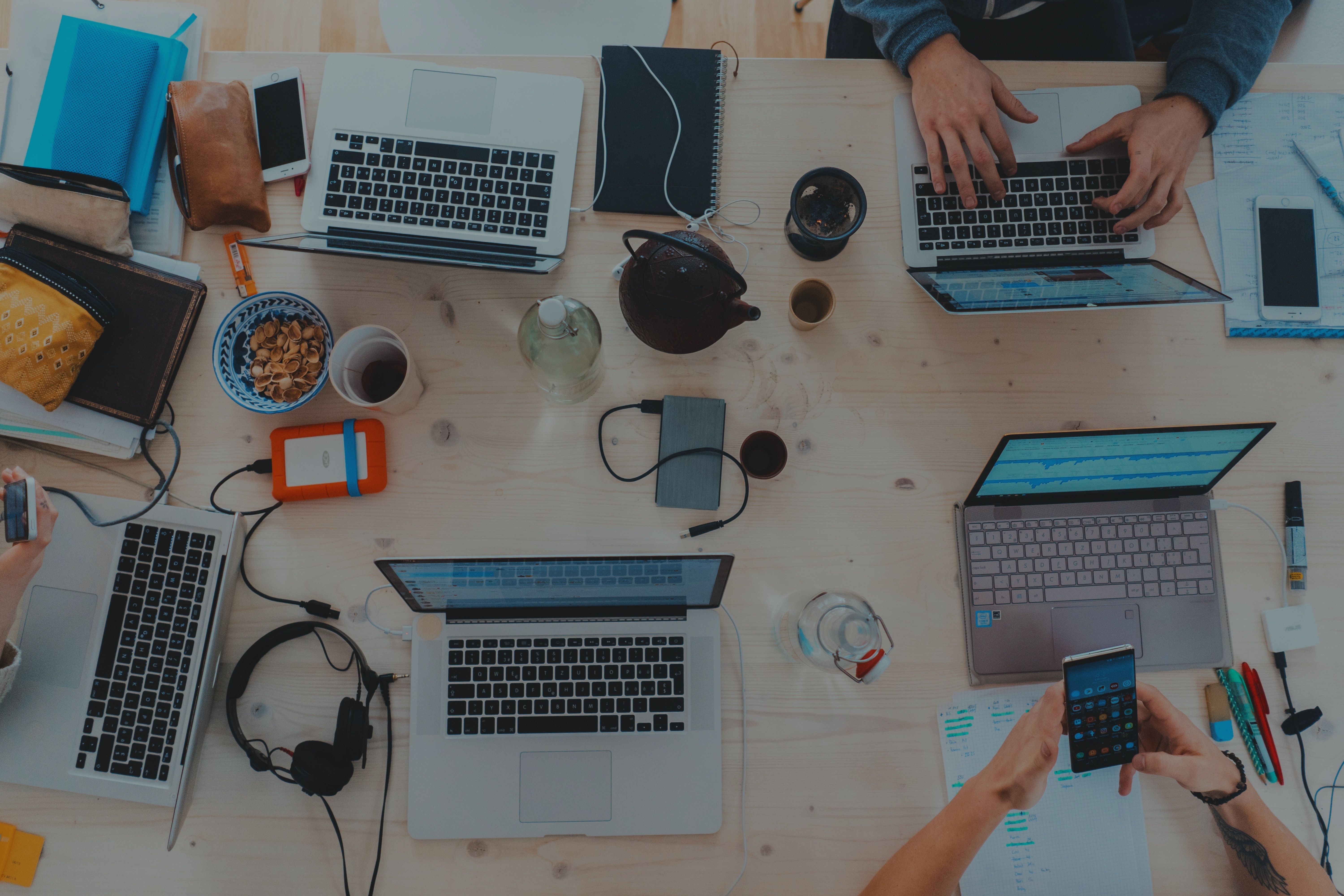 Table cluttered with laptops, cell phones, pens, and snacks