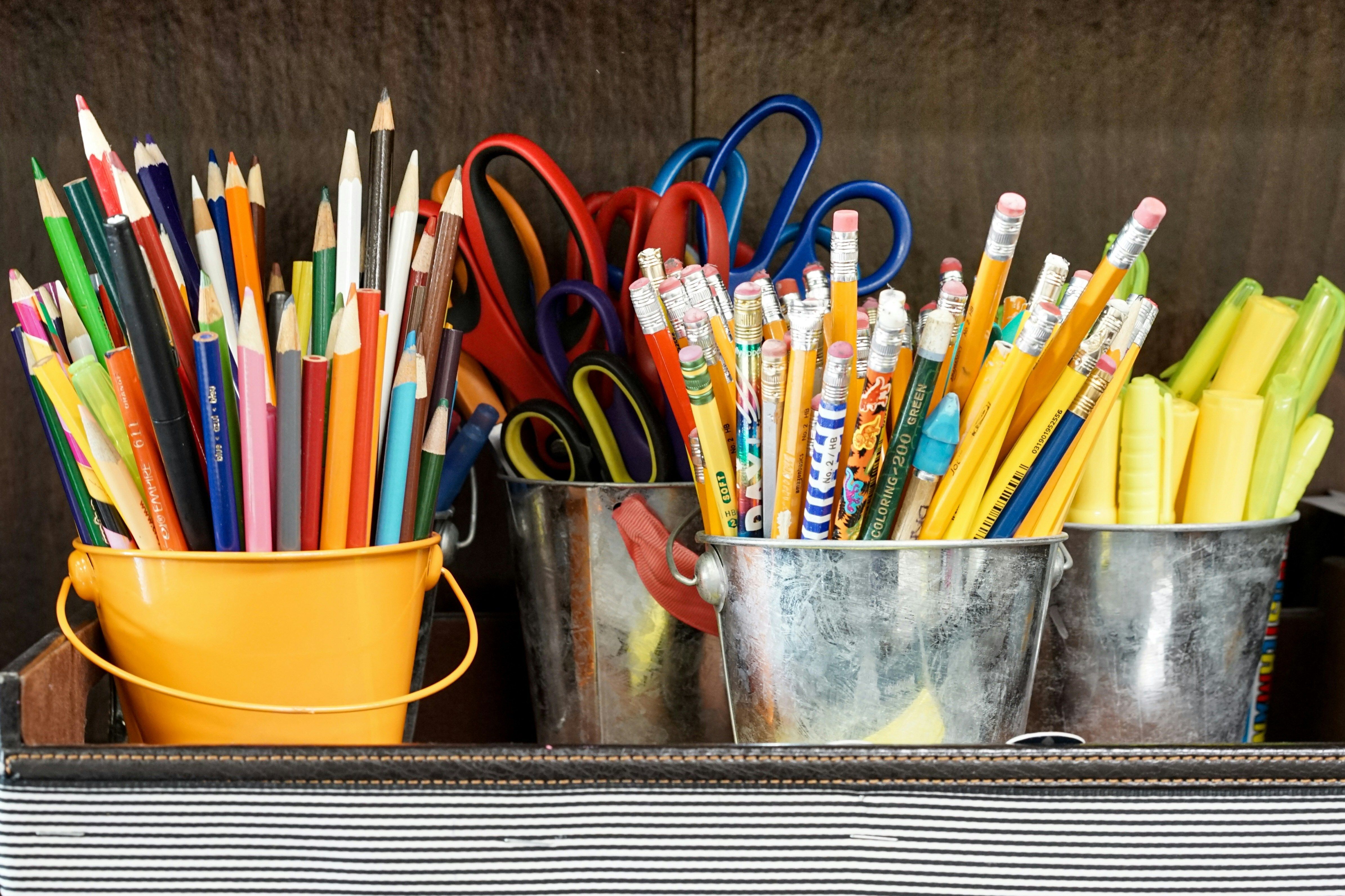 Multiple cups of writing implements like crayons, colored pencils, highlighters, and scissors.