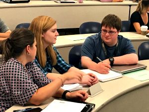 Three students, one with a disability, sit in classroom doing group work