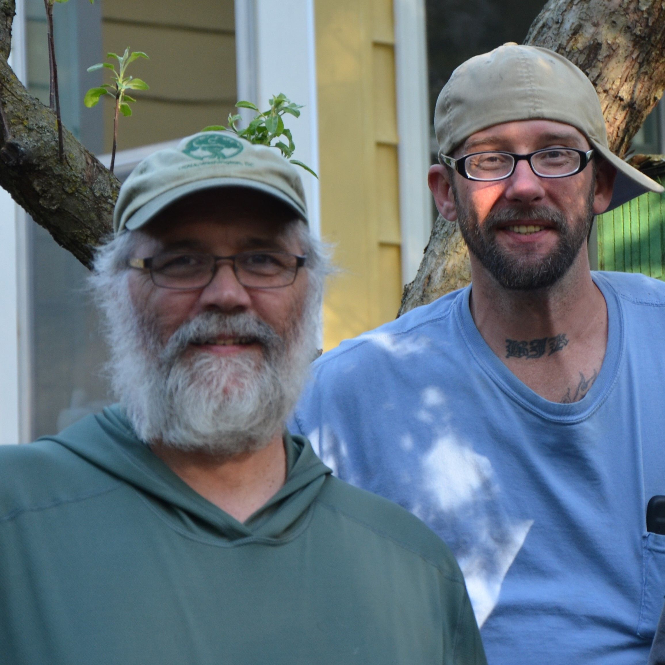 Richard Gagne in a green shirt and baseball cap stands with a Dismas resident in a blue shirt and sideways baseball cap.