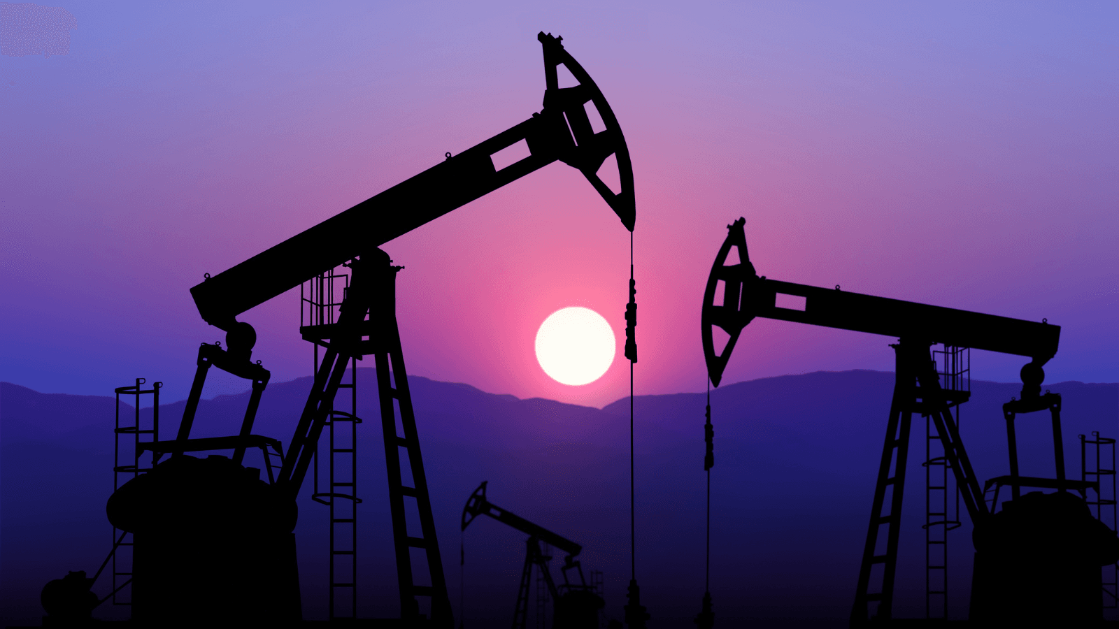Oil wells in front of setting sun over mountains