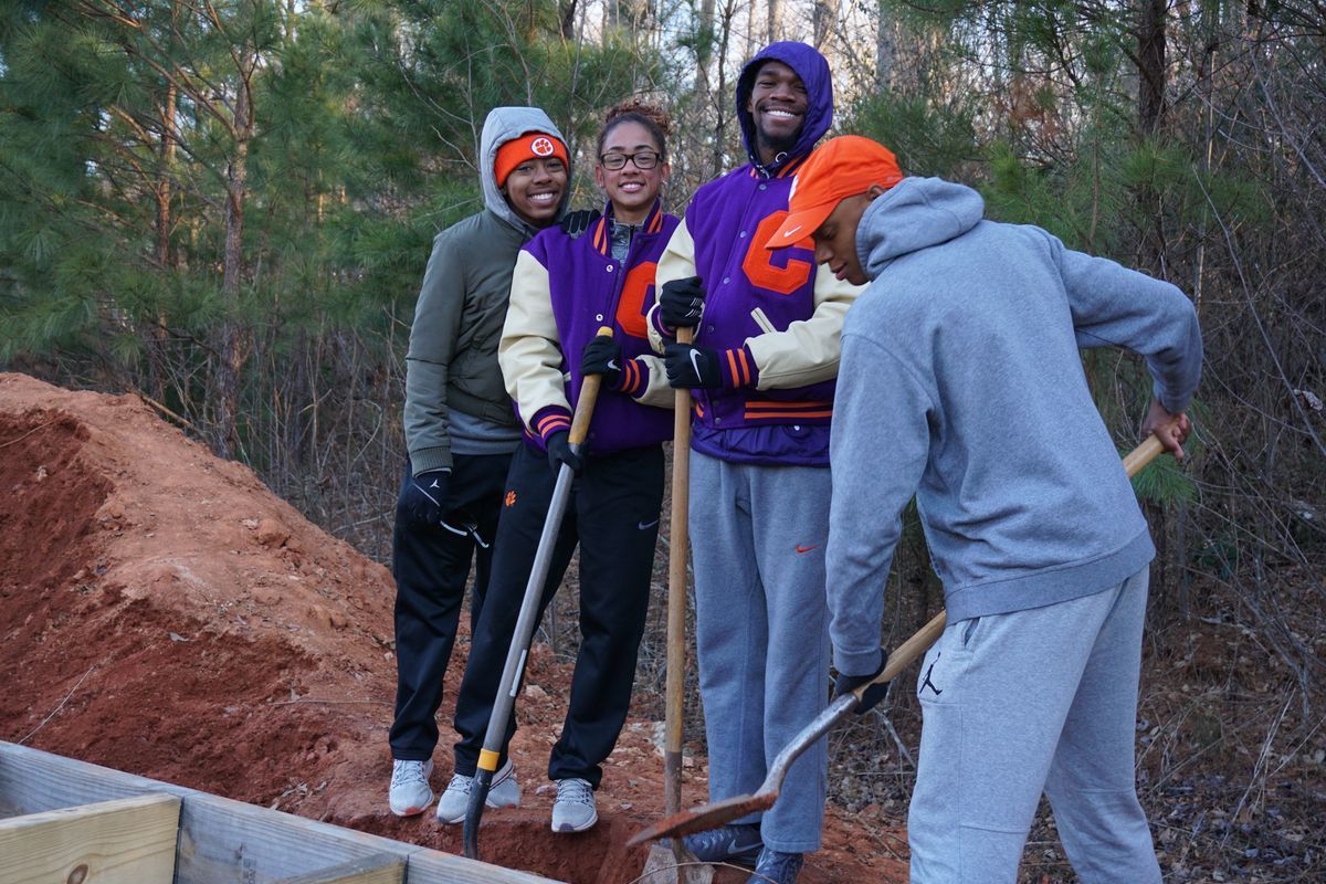 Four track athletes hold shovels on the construction site. 