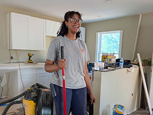 Volunteer smiling while holding a broom in a kitchen under renovation