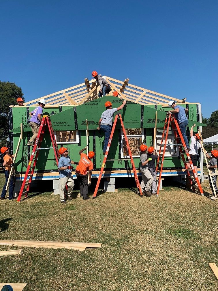 Students wear hard hats - some on ladders - as they build the 2021 Homecoming house.