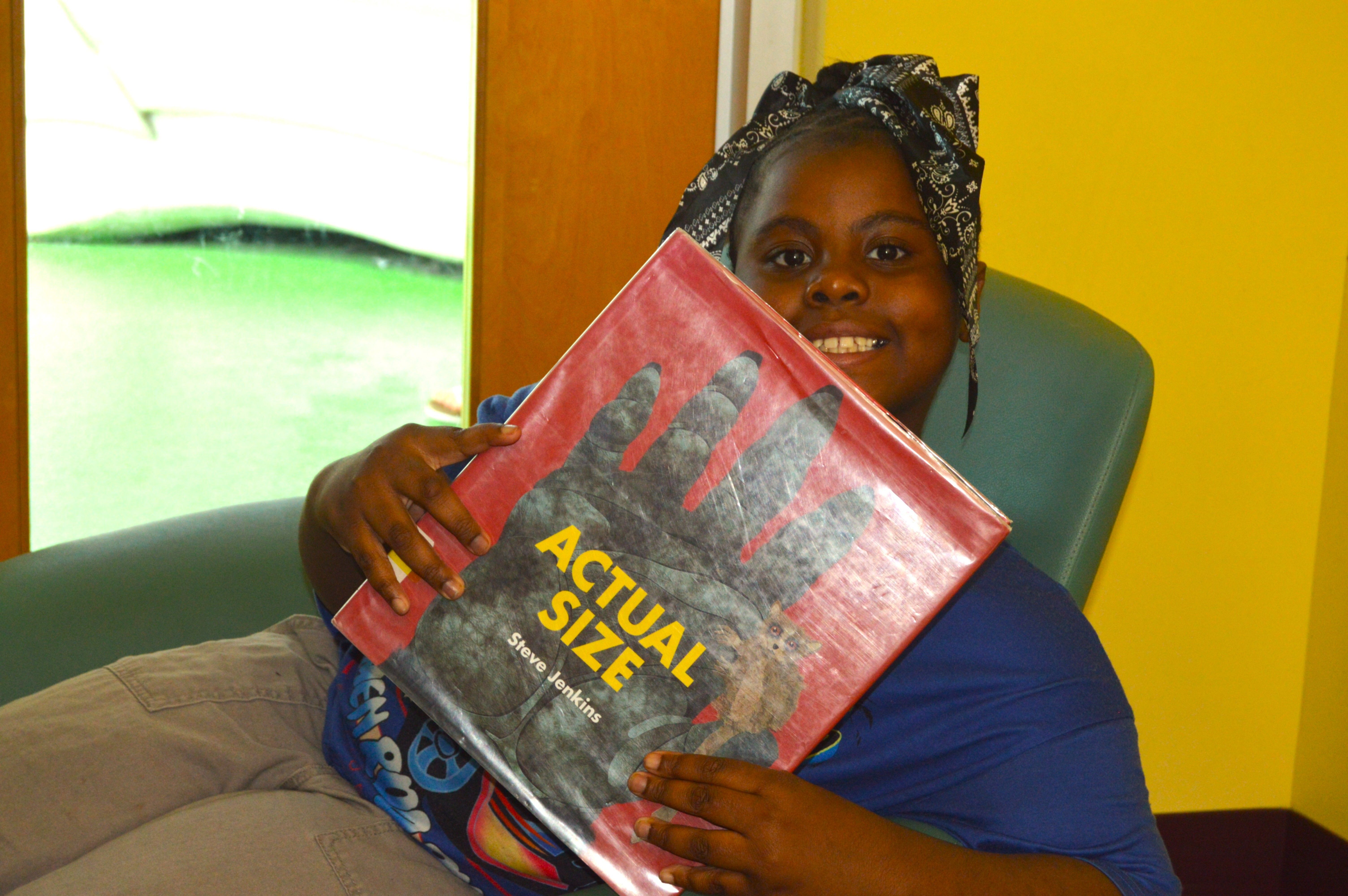 Smiling child holds up a book she has read at Boys & Girls Club.
